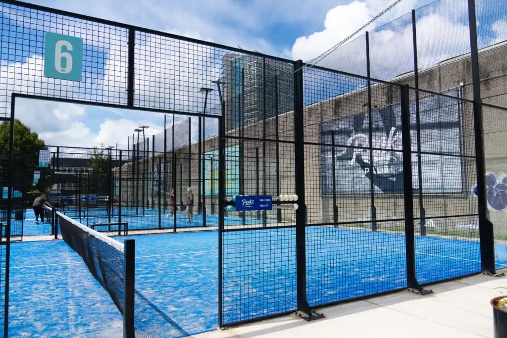 Outdoor padelbaan met glazen kooiconstructie tegen een blauwe lucht