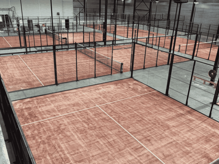6 indoor padelbanen met terracotta kunstgras en zwarte kooien bij TRES Amstelveen.
