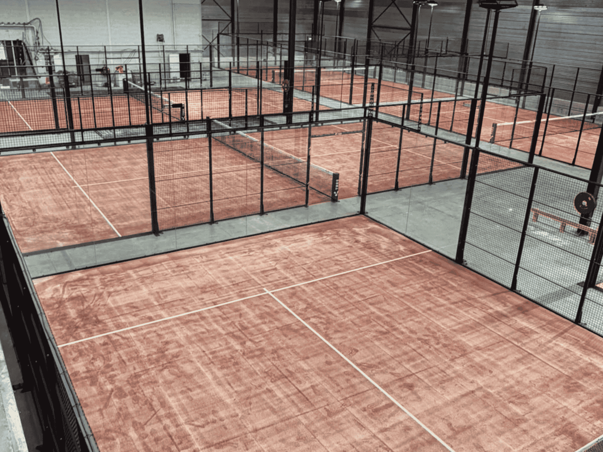 6 indoor padelbanen met terracotta kunstgras en zwarte kooien bij TRES Amstelveen.